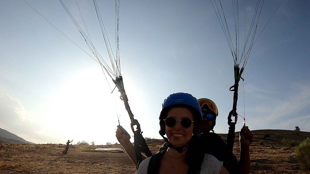 Two people paragliding with a clear sky and a hilly landscape in the background. 5