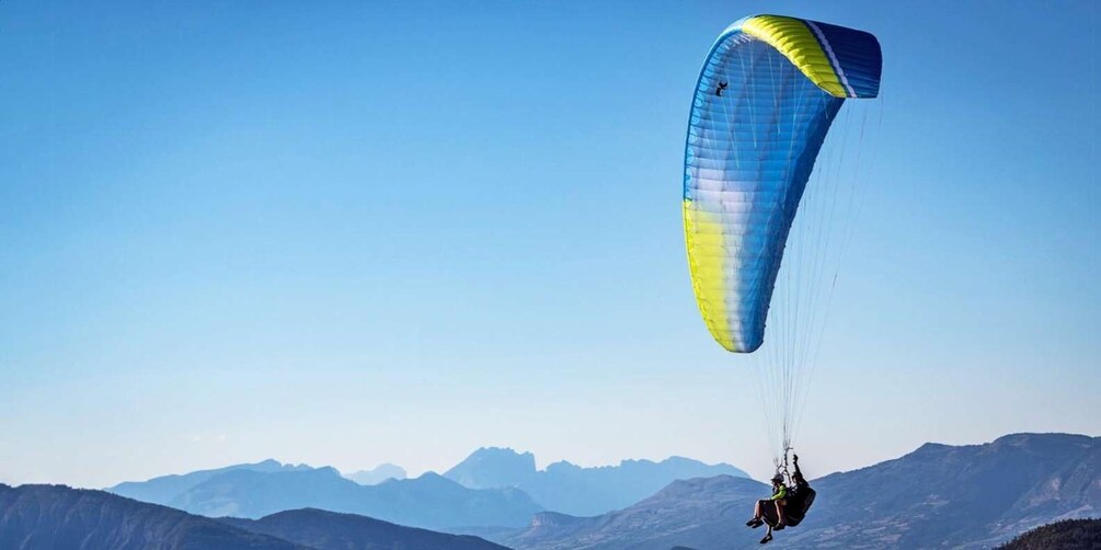 A person paragliding with a blue and yellow parachute over a mountainous landscape. 1