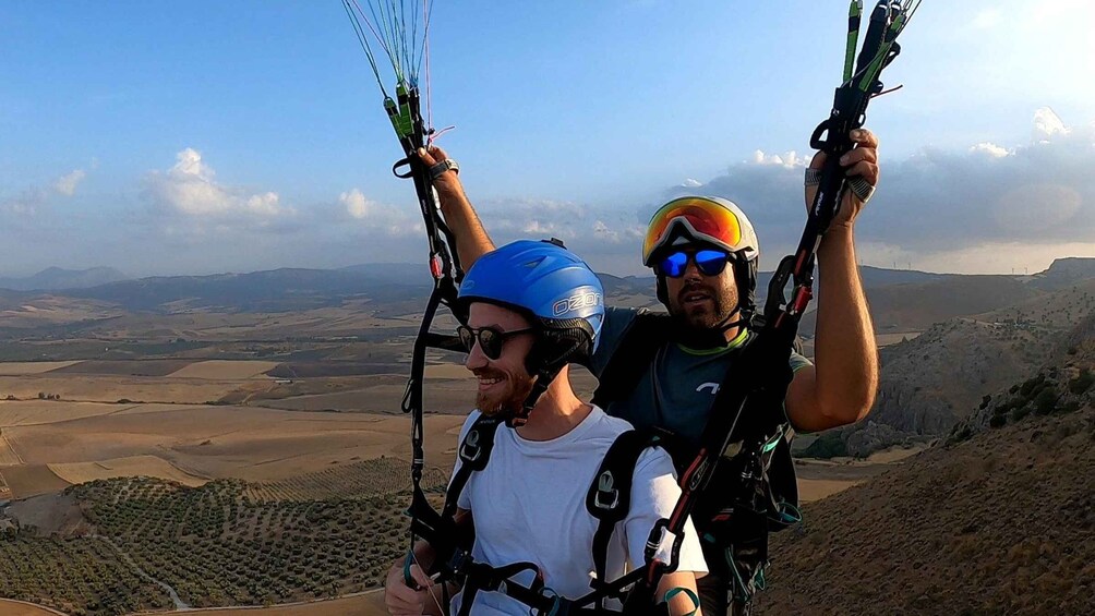 Two people paragliding with a vast landscape in the background. 3