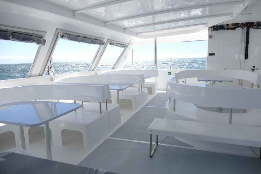A boat deck with white tables and chairs, large windows, and a view of the ocean. 3