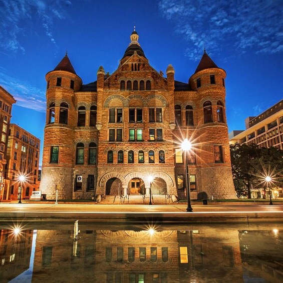 A historic building with arched windows and a central tower, reflecting in a water body in front. 1