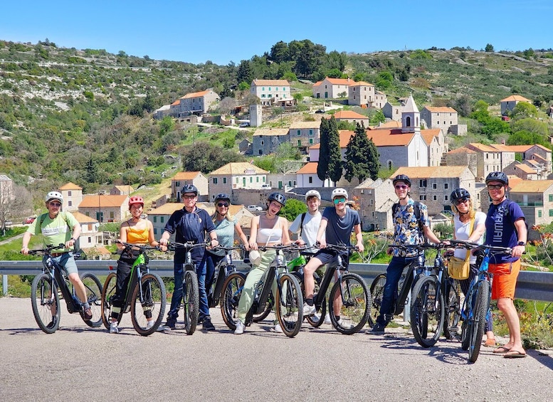 A group of cyclists on a paved path with a scenic view of a hilly town in the background. 4