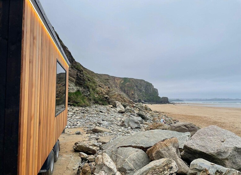A wooden structure with a glass window, a rocky beach, and a cliff. 2