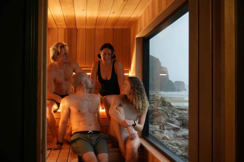 A sauna with wooden walls and a large window overlooking a rocky beach. 3