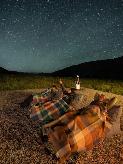 Two people lying on a gravel surface under a starry night sky, with a telescope in the background. 5