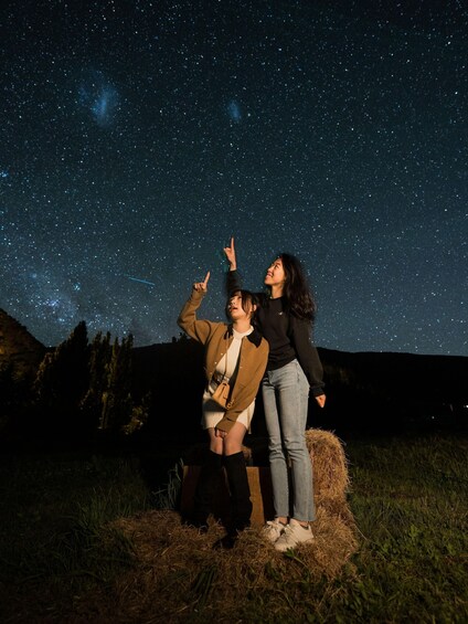 Two people standing on a hay bale under a starry night sky. 2