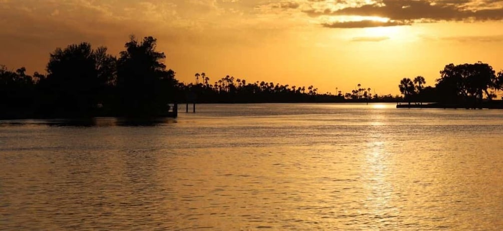A sunset over a calm body of water with silhouettes of trees and a pier. 1