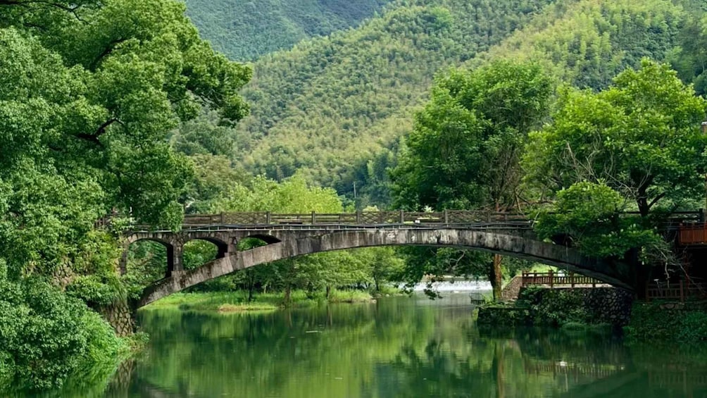 A stone bridge over a calm river, surrounded by lush greenery and hills. 1