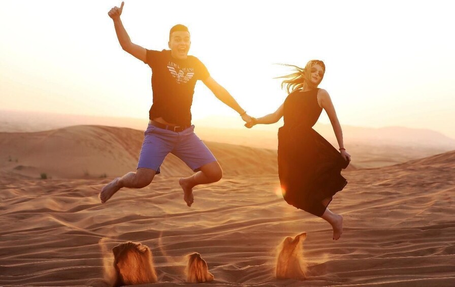 Two people jumping in a desert with sand dunes in the background. 4