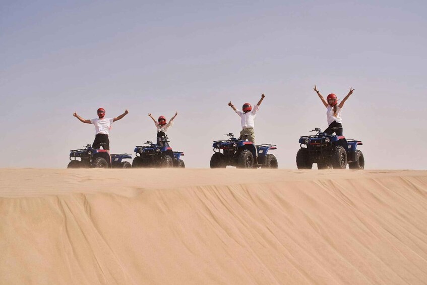 Four people on quad bikes in a desert with sand dunes. 3