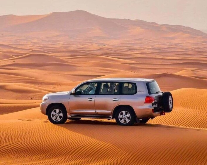 A silver SUV parked on a sand dune with a desert landscape in the background. 2