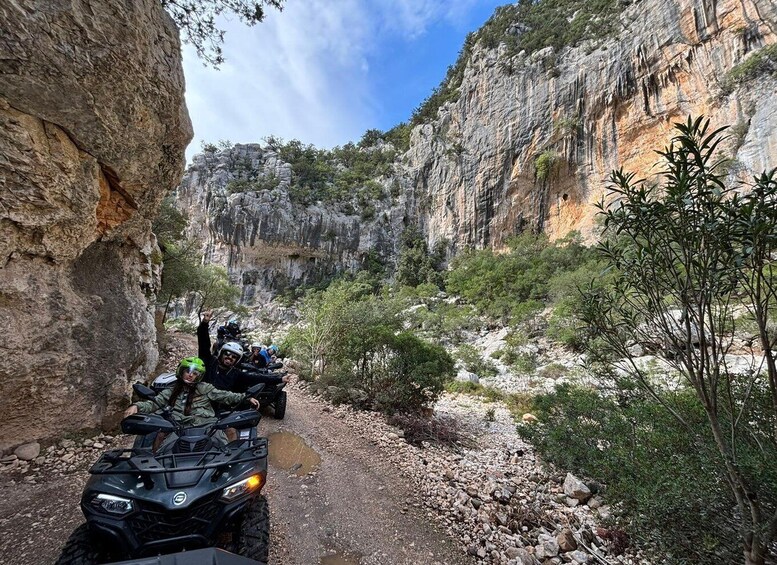 A group of people on ATVs navigating a rocky canyon with steep cliffs and sparse vegetation. 3