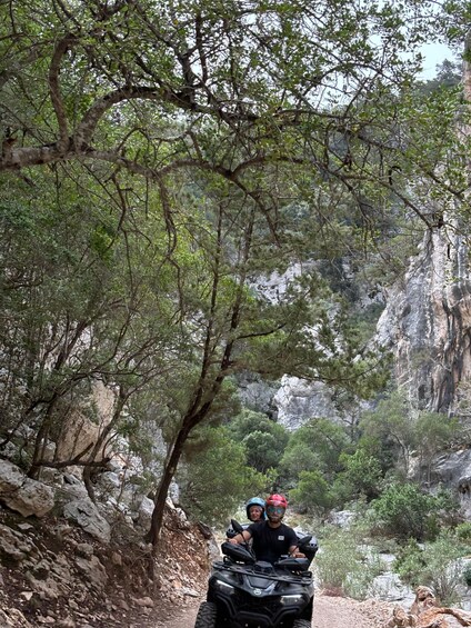 Two people on an ATV in a rocky canyon with trees. 2