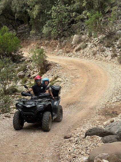 Two people on an ATV on a rocky trail surrounded by greenery. 5