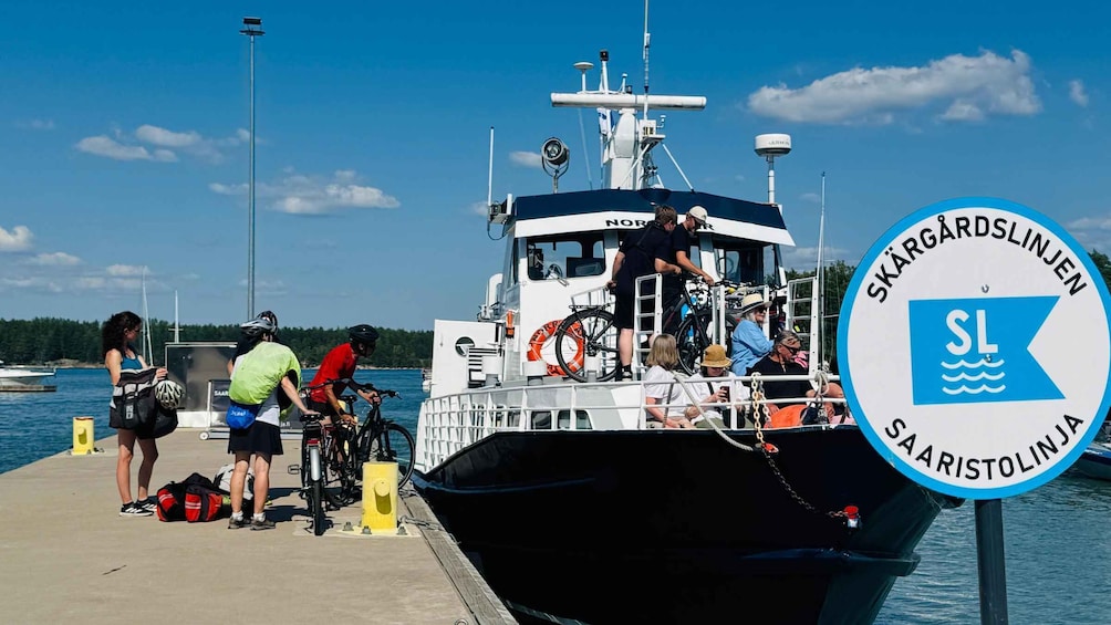A ferry dock with people boarding a boat, bicycles, and a sign indicating 'Skärgårdslinjen' and 'Saaristolinja'. 4