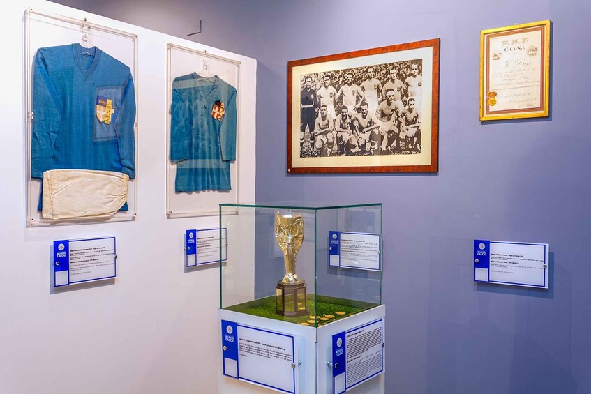 A museum exhibit with sports jerseys, a framed photograph, a trophy, and informational plaques. 1