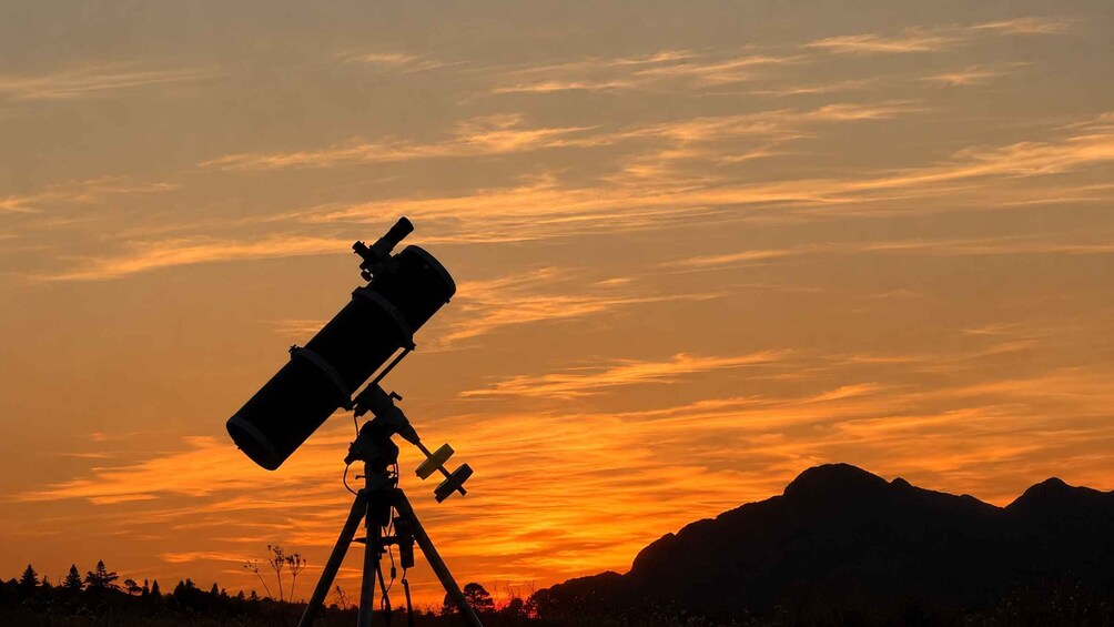 A telescope against a sunset sky with mountains in the background. 1