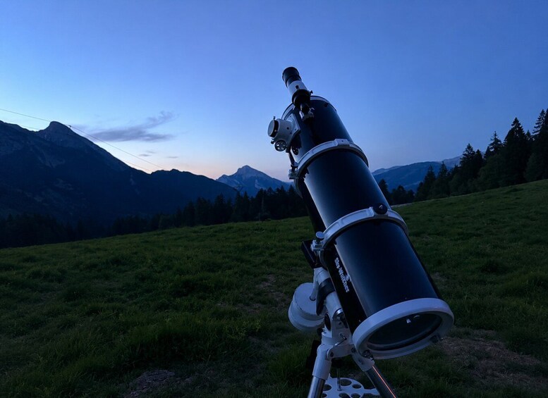 A telescope in a grassy field with mountains in the background. 3