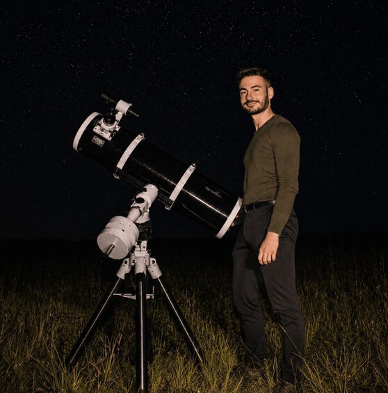 A person standing next to a large telescope on a tripod in a grassy field under a starry night sky. 2