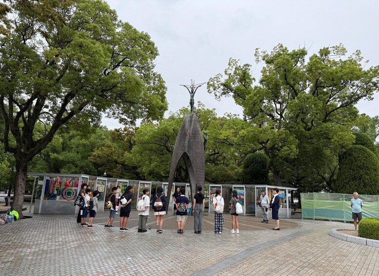 A group of people standing in a park with a tall, narrow monument in the center. 2