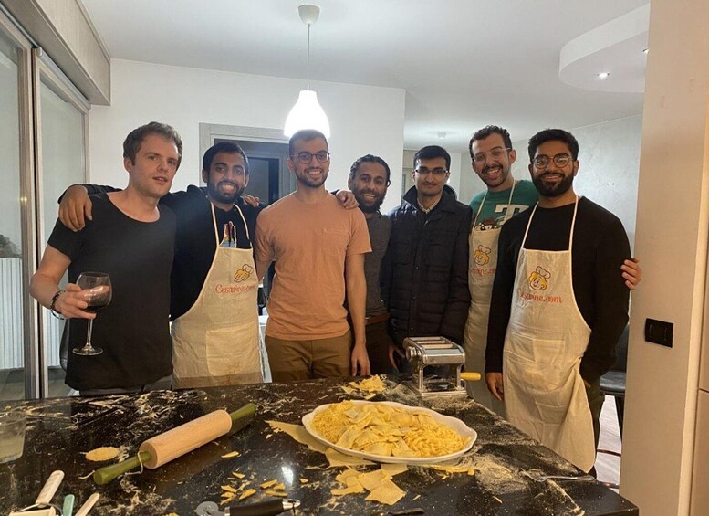 A group of people in a kitchen with a marble countertop, a rolling pin, a plate of pasta, and a pasta machine. 5