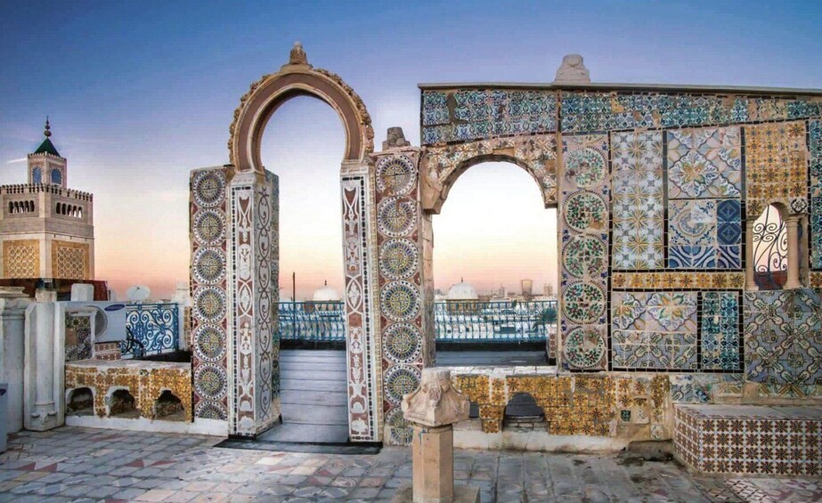 A historic gate with intricate tile work, a domed building, and a cityscape in the background. 3