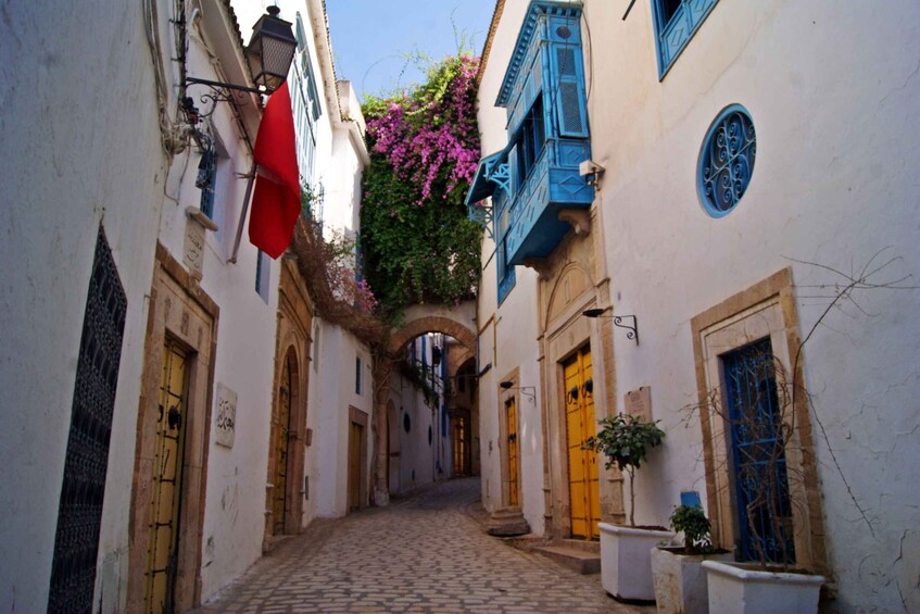 A narrow cobblestone alley with buildings on either side, some with blue shutters and others with yellow doors. 2