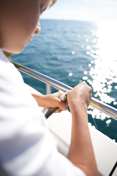 A person holding a fishing rod over the side of a boat, with the ocean in the background. 3