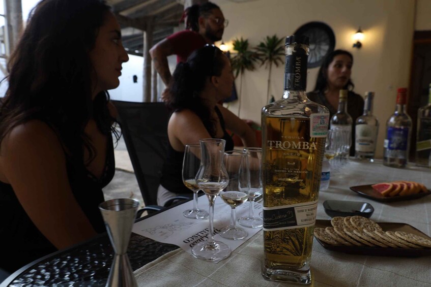 A group of people sitting at a table with a bottle of Trombá tequila and glasses. 2