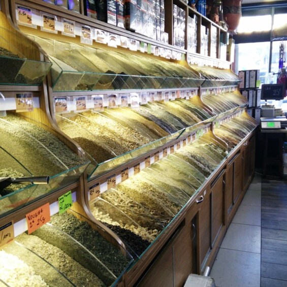 A store aisle with glass-fronted bins filled with various grains and seeds, each labeled with prices. 5