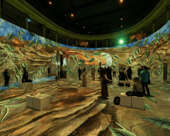 An indoor exhibition space with a mural of a forest scene, people observing exhibits, and a stage area. 4