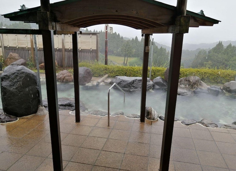 A stone hot spring area with a wooden pavilion and large rocks. 5