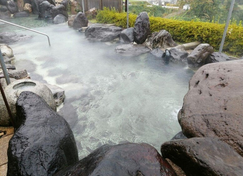 A hot spring area with large rocks and a metal railing. 1