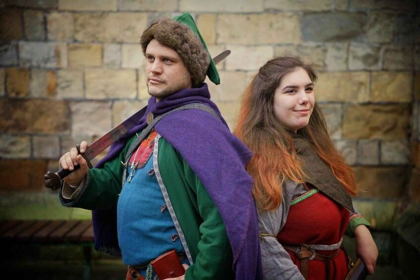 A person in a green and purple costume holding a sword, standing next to a person in a red dress. 1