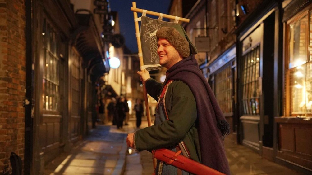 A person in medieval costume holding a staff with a leaf design, walking down a narrow street at night. 5