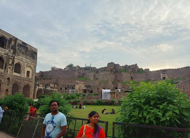 An ancient fort with arched windows and a large wall, surrounded by greenery and visitors. 4