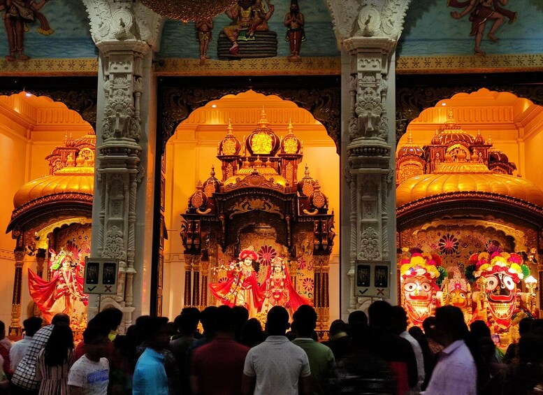 A temple interior with ornate carvings, a central deity statue, and a crowd of people. 3