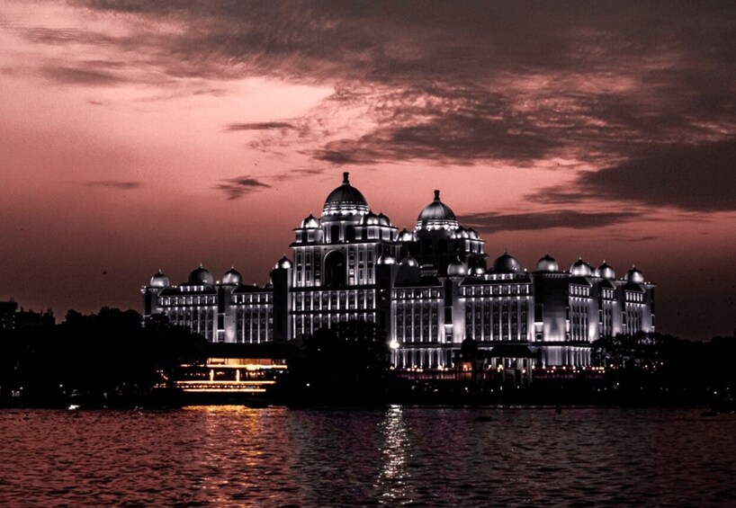 A grand, illuminated building with multiple domes, reflecting on the water surface at dusk. 1
