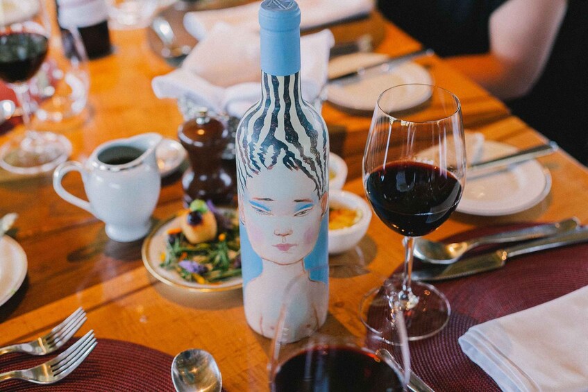 A table with a bottle, a glass of red wine, and various dishes. 1