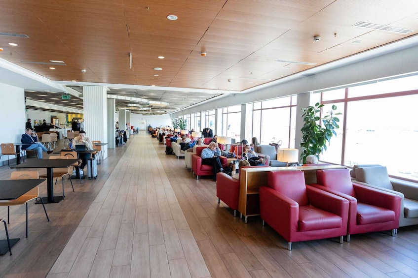 A spacious indoor area with wooden flooring, red seating, and large windows allowing natural light. 3