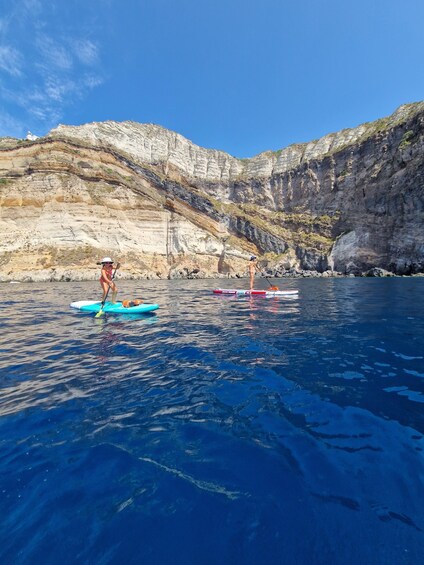 Two paddleboarders on a calm sea with rocky cliffs in the background. 2