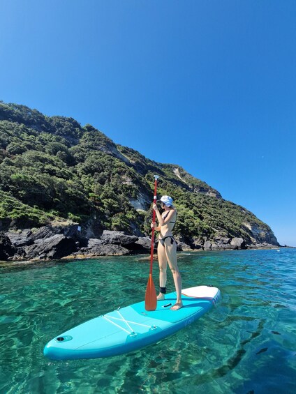A person paddleboarding on clear turquoise water with a mountainous backdrop. 1