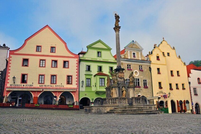 A cobblestone square with colorful buildings, a statue, and a fountain. 2