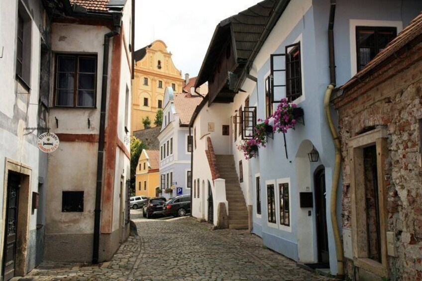 A cobblestone street lined with historic buildings, a parked car, and a staircase leading to an upper level. 5