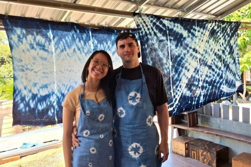 Two people wearing blue aprons with white patterns, standing in front of a blue and white patterned cloth. 5