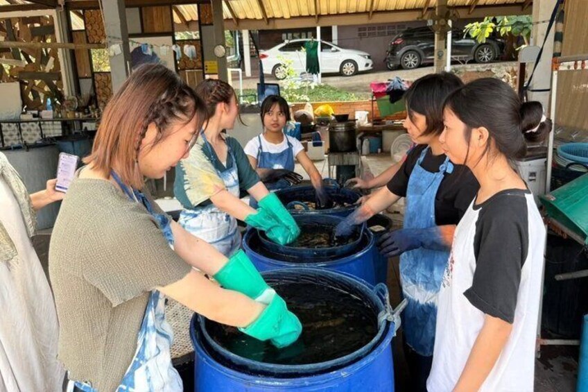 People wearing aprons and gloves, working with large blue containers, likely in a workshop or industrial setting. 4
