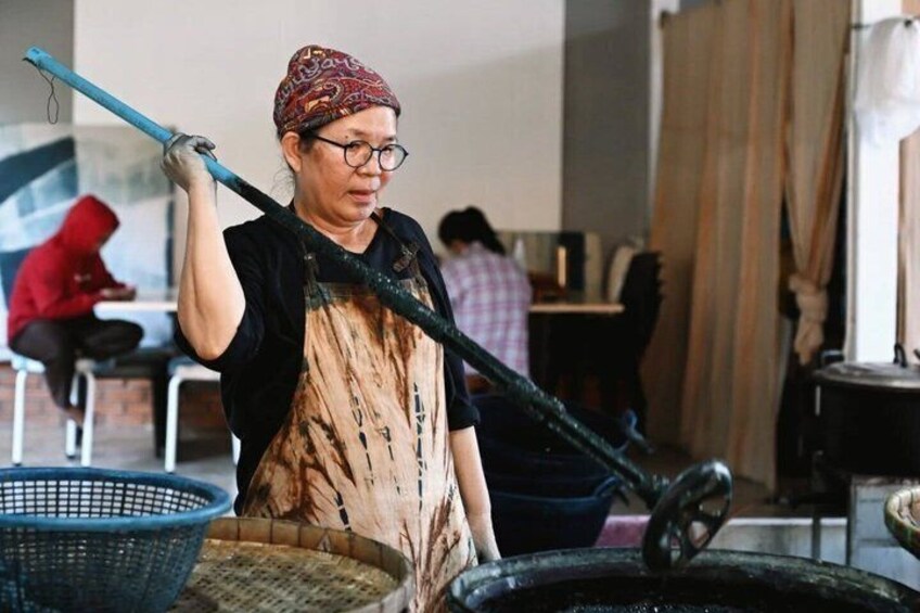 A person operating a large black industrial machine, possibly for processing or manufacturing, in an indoor setting with other individuals in the background. 3