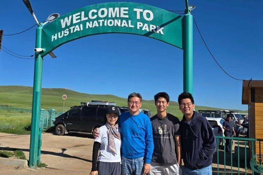 A group of people standing under a sign that reads 'WELCOME TO HUSTAI NATIONAL PARK.' 1