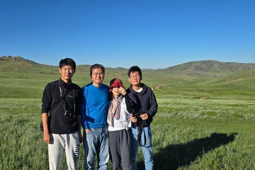 Four people standing in a grassy field with mountains in the background. 4
