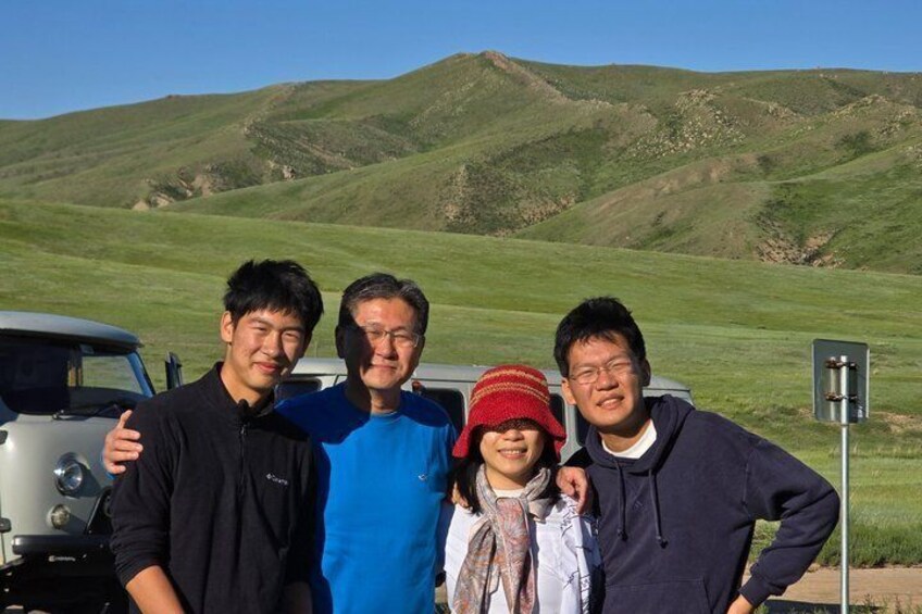 A group of people standing in front of a vehicle with a hilly landscape in the background. 5
